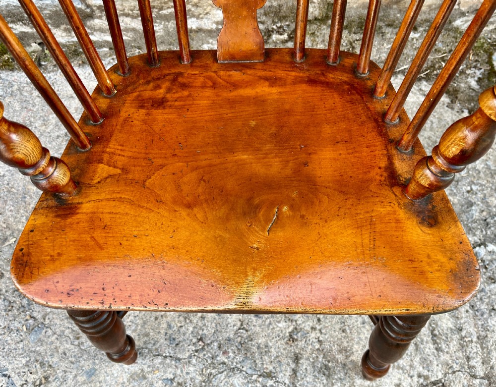 A warm brown wooden Windsor armchair featuring a curved hoop back, central pierced splat, turned spindles, shaped armrests, turned legs, and a crinoline stretcher. View IV