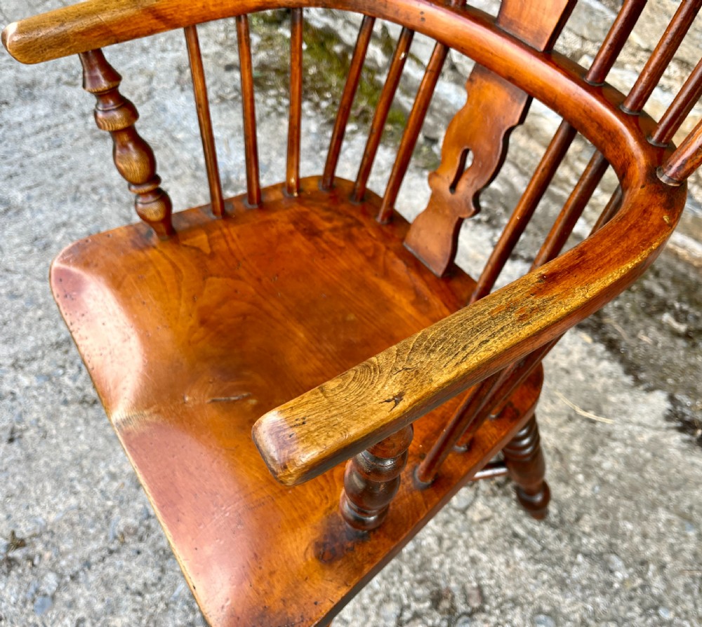 A warm brown wooden Windsor armchair featuring a curved hoop back, central pierced splat, turned spindles, shaped armrests, turned legs, and a crinoline stretcher. View V
