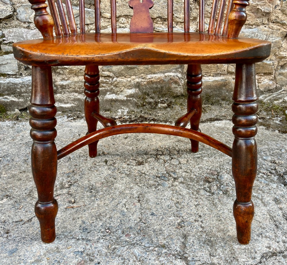 A warm brown wooden Windsor armchair featuring a curved hoop back, central pierced splat, turned spindles, shaped armrests, turned legs, and a crinoline stretcher. View VI