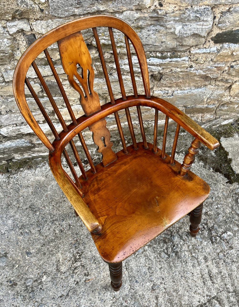 A warm brown wooden Windsor armchair featuring a curved hoop back, central pierced splat, turned spindles, shaped armrests, turned legs, and a crinoline stretcher. View XI