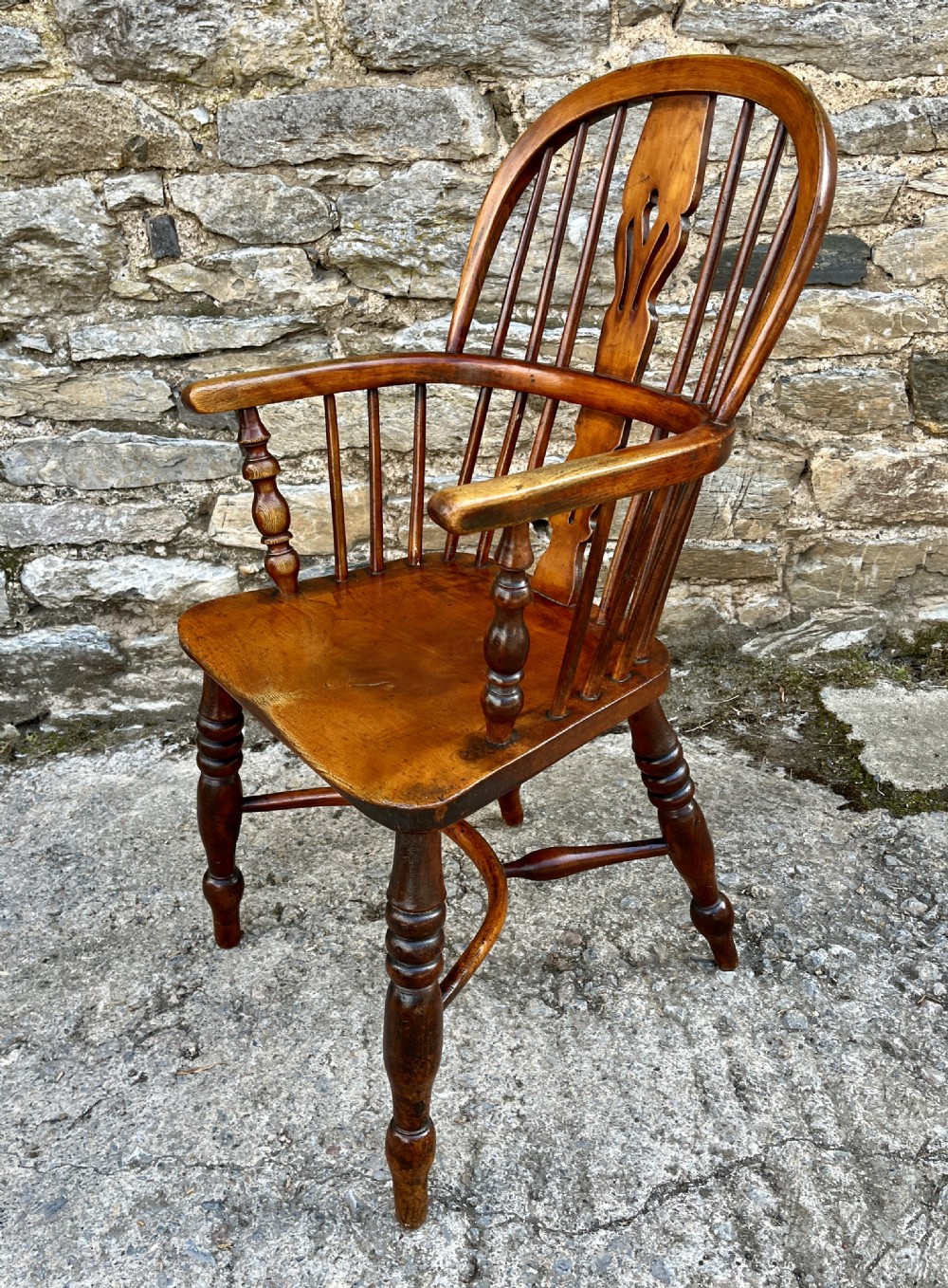 A warm brown wooden Windsor armchair featuring a curved hoop back, central pierced splat, turned spindles, shaped armrests, turned legs, and a crinoline stretcher. View XIII