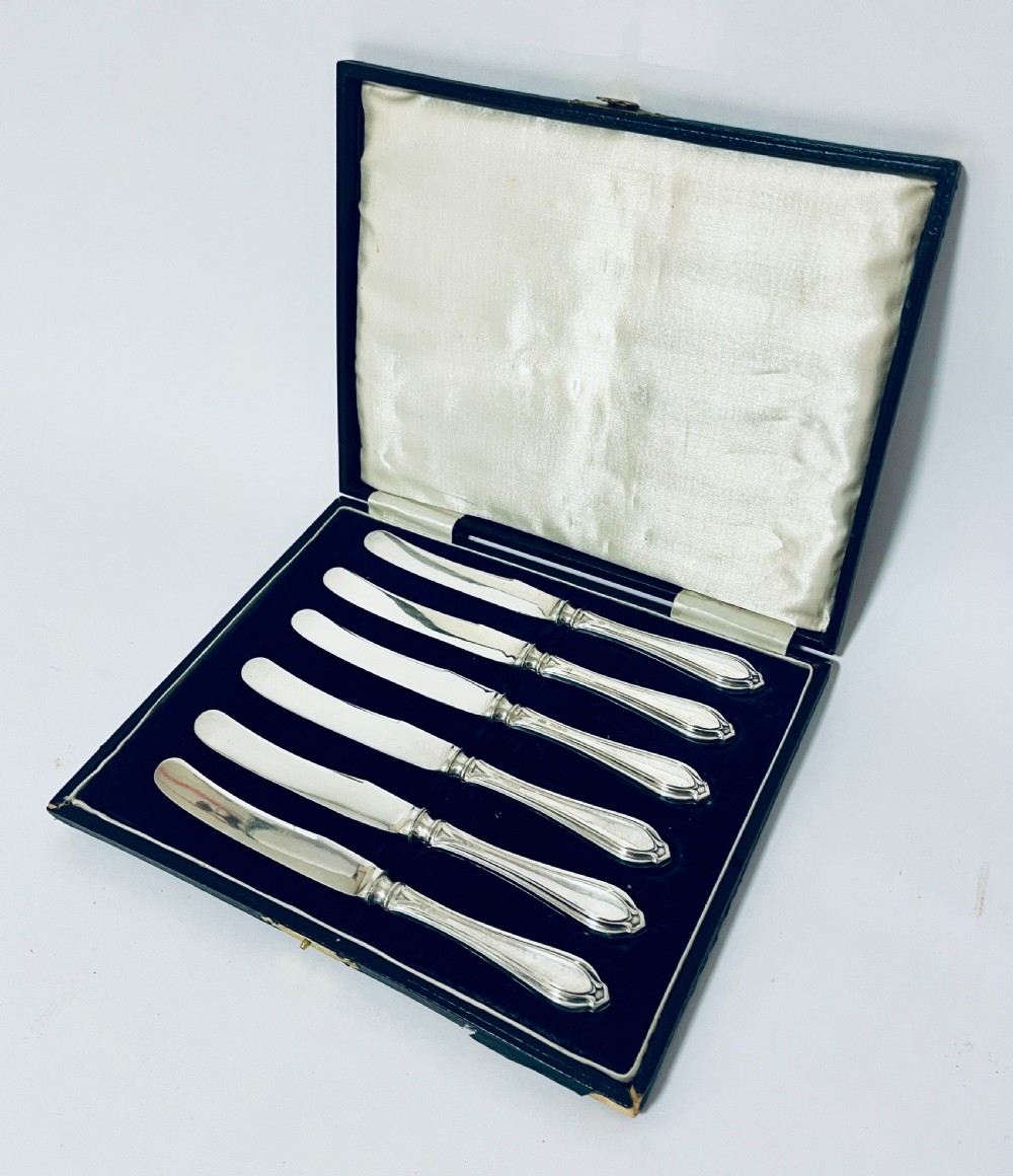 A set of six silver-handled butter knives arranged in a dark velvet and cream satin-lined presentation box. View II