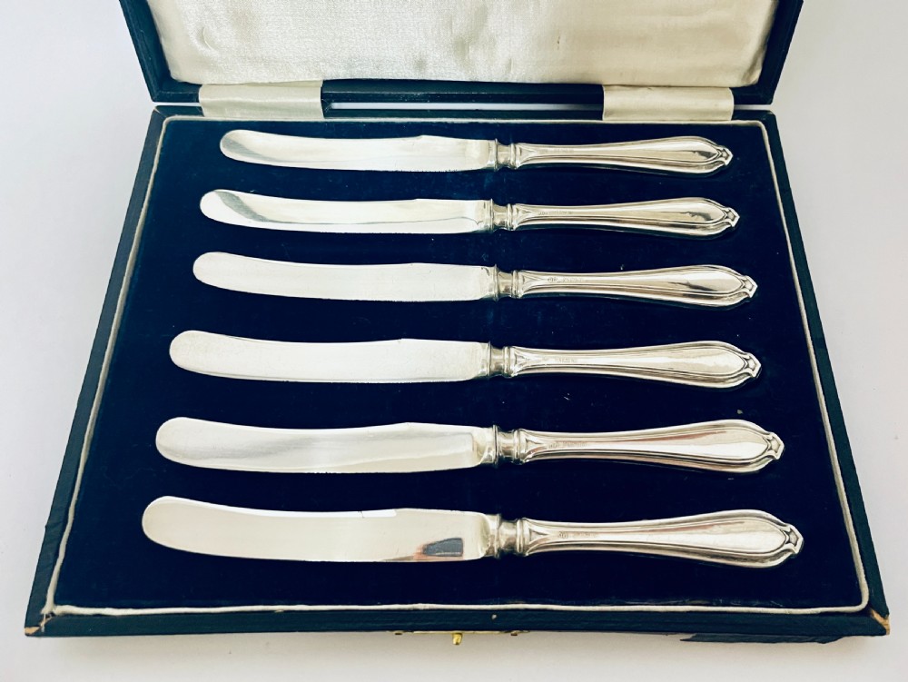 A set of six silver-handled butter knives arranged in a dark velvet and cream satin-lined presentation box. View III