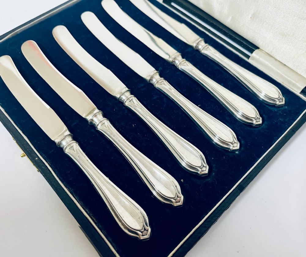 A set of six silver-handled butter knives arranged in a dark velvet and cream satin-lined presentation box. View IV