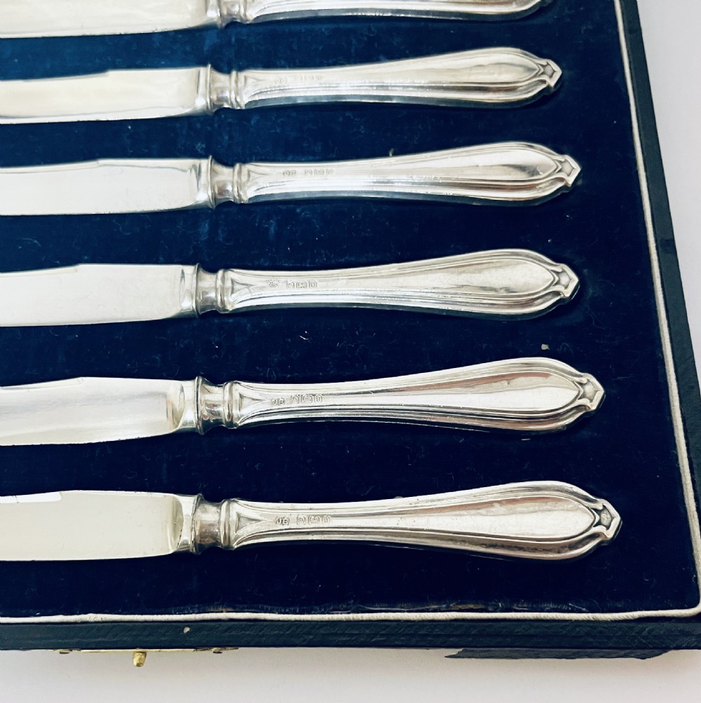 A set of six silver-handled butter knives arranged in a dark velvet and cream satin-lined presentation box. View V