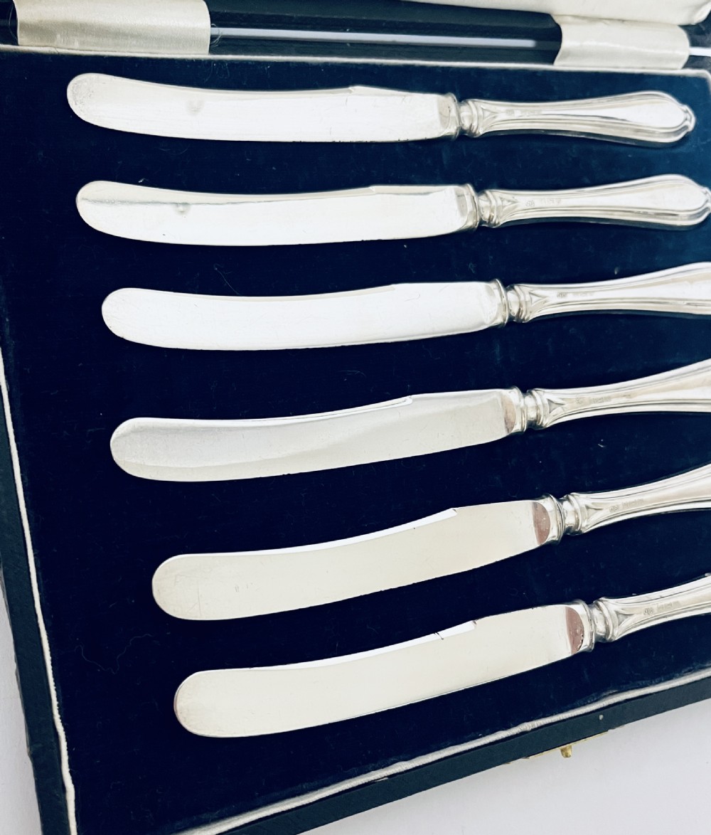 A set of six silver-handled butter knives arranged in a dark velvet and cream satin-lined presentation box. View VI
