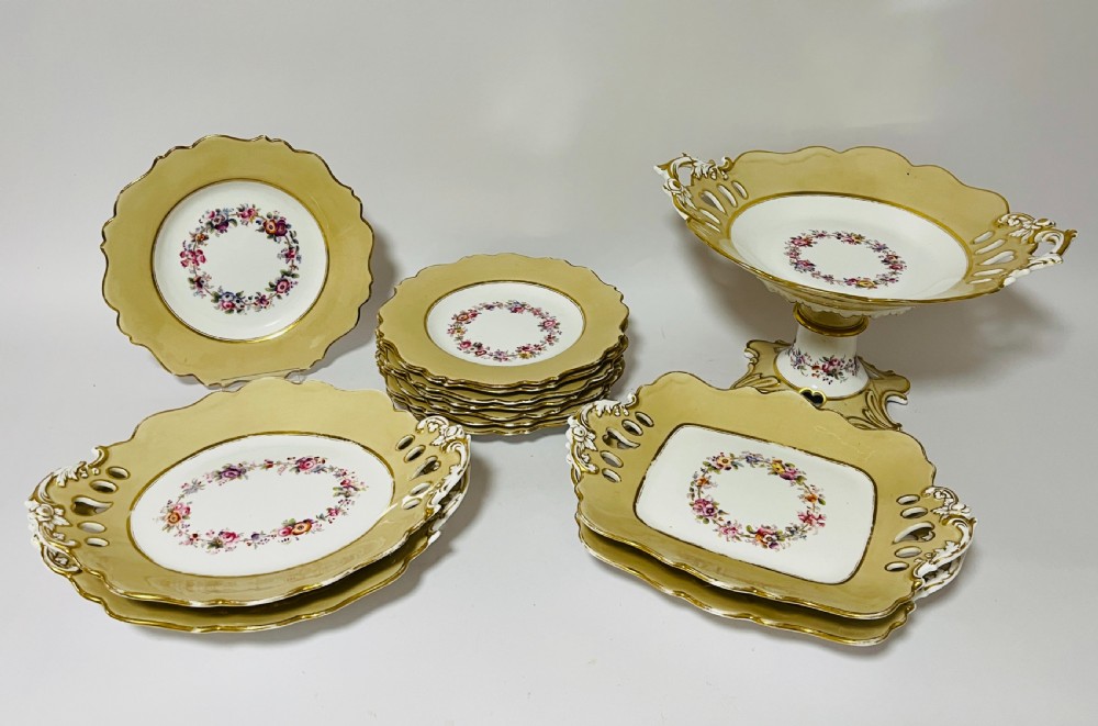 A nineteenth-century John Ridgway porcelain dessert service featuring buff-coloured borders, gilded scrollwork, reticulated handles, and hand-painted central floral garlands.