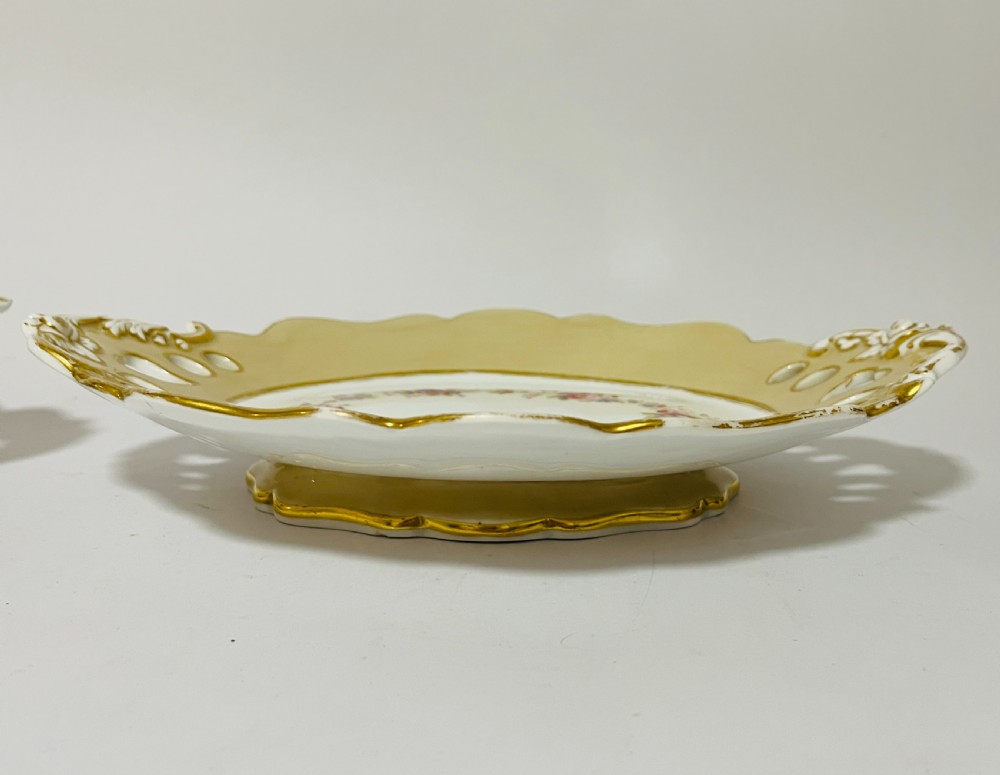 A nineteenth-century John Ridgway porcelain dessert service featuring buff-coloured borders, gilded scrollwork, reticulated handles, and hand-painted central floral garlands. View VI