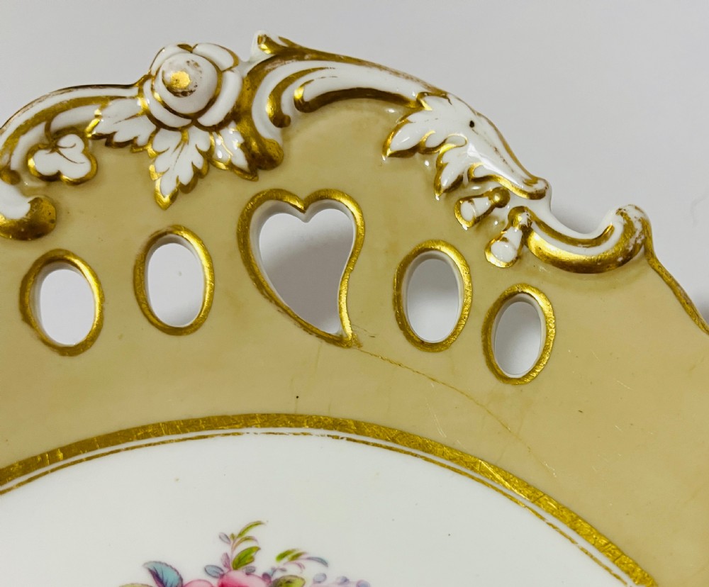 A nineteenth-century John Ridgway porcelain dessert service featuring buff-coloured borders, gilded scrollwork, reticulated handles, and hand-painted central floral garlands. View VIII