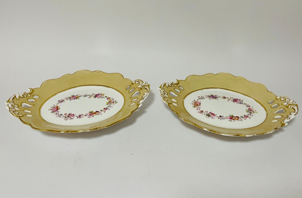 A nineteenth-century John Ridgway porcelain dessert service featuring buff-coloured borders, gilded scrollwork, reticulated handles, and hand-painted central floral garlands. View XV