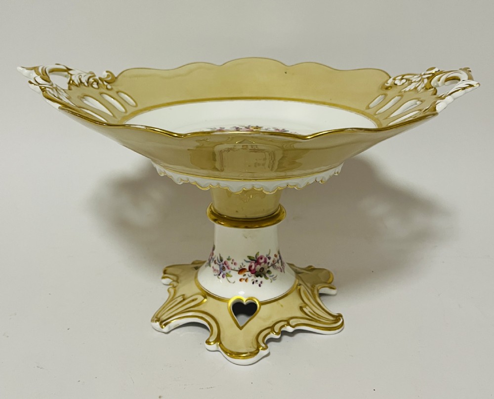 A nineteenth-century John Ridgway porcelain dessert service featuring buff-coloured borders, gilded scrollwork, reticulated handles, and hand-painted central floral garlands. View XVI