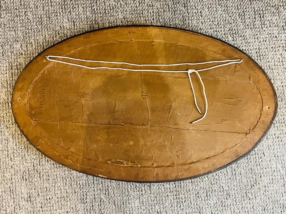An oval Arts and Crafts wall mirror with a hand-hammered copper frame featuring embossed floral motifs at four points and a bevelled glass edge. View VI