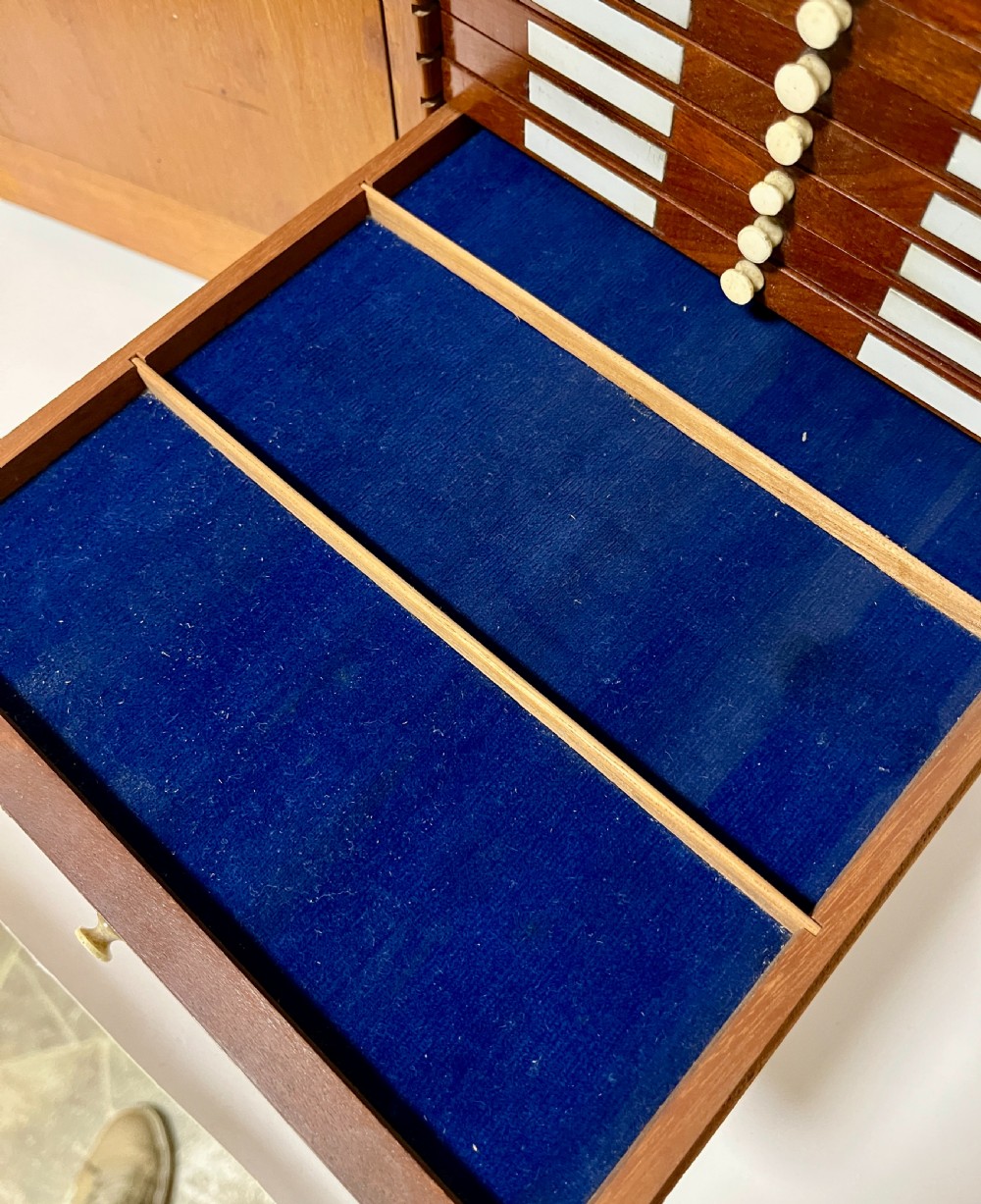 A warm brown wooden microscope slide cabinet with its single door open to reveal numerous shallow horizontal drawers with small round pulls. View III