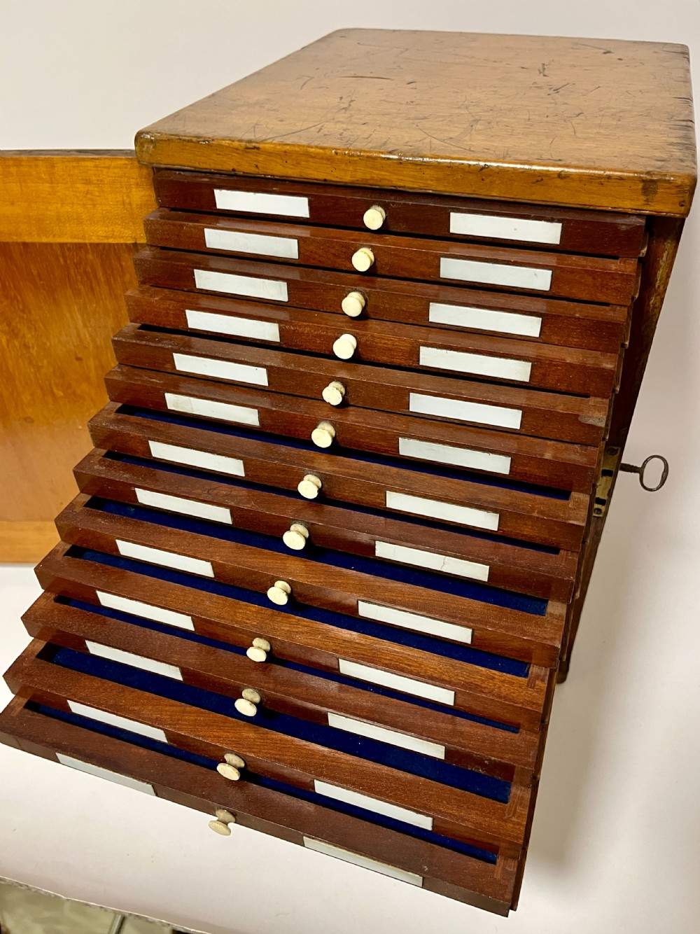 A warm brown wooden microscope slide cabinet with its single door open to reveal numerous shallow horizontal drawers with small round pulls. View IV