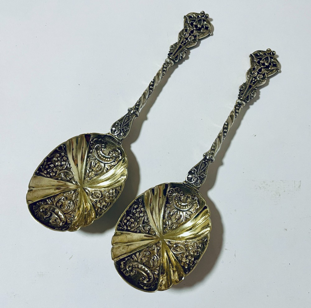A pair of Victorian silver-gilt serving spoons featuring fluted embossed bowls with scroll patterns and twisted handles.