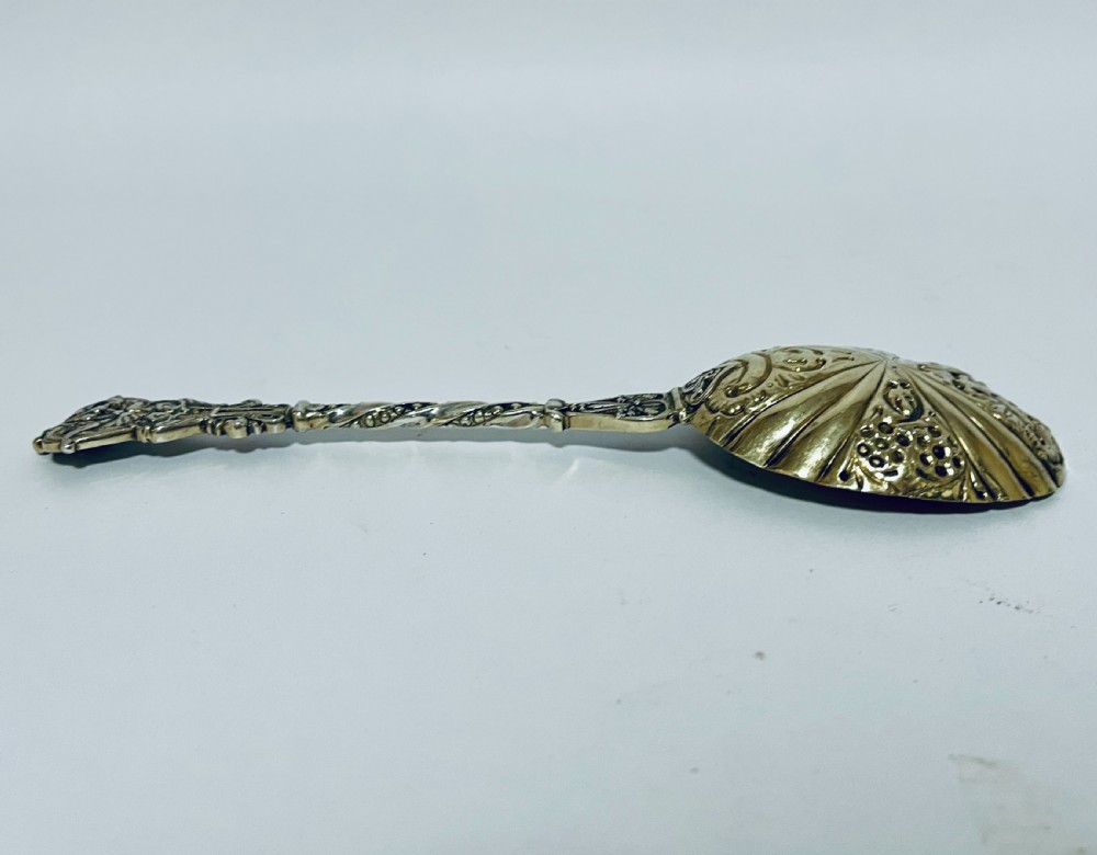 A pair of Victorian silver-gilt serving spoons featuring fluted embossed bowls with scroll patterns and twisted handles. View X