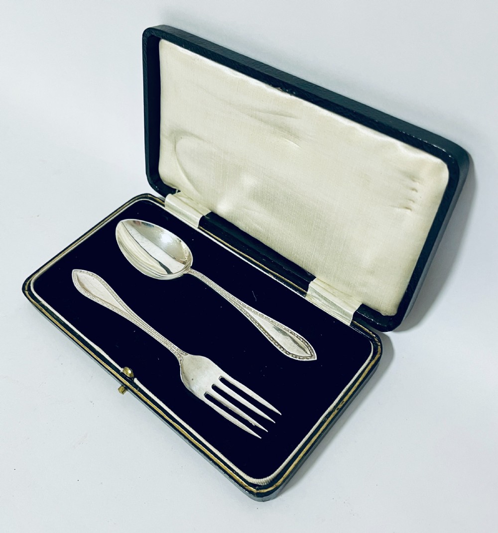 An antique silver christening spoon and fork set presented inside an open black fitted case lined with cream silk and dark velvet. View II