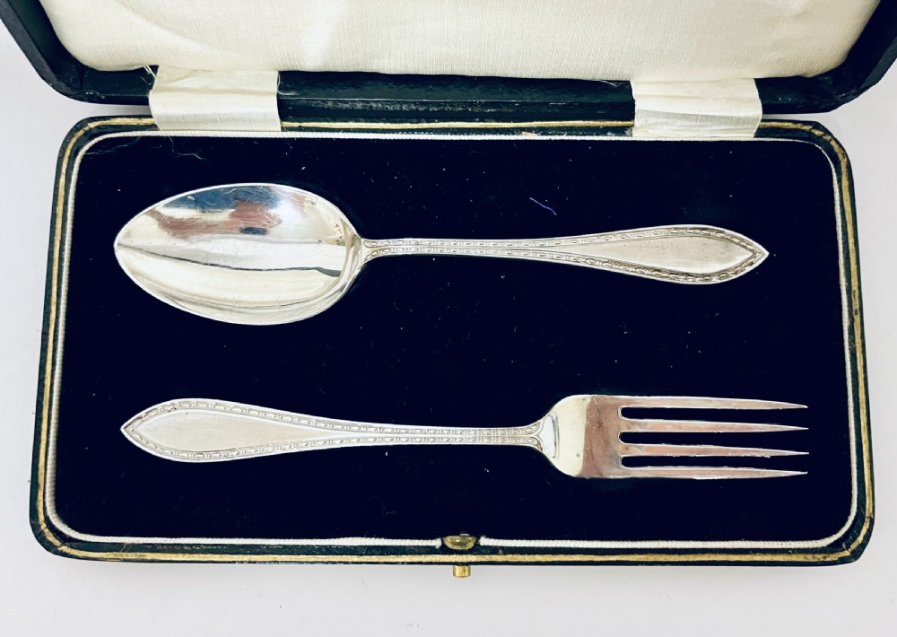 An antique silver christening spoon and fork set presented inside an open black fitted case lined with cream silk and dark velvet. View III