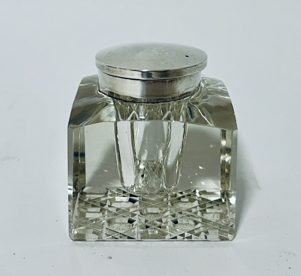 A square cut glass inkwell featuring a circular silver cap and diamond-patterned base.