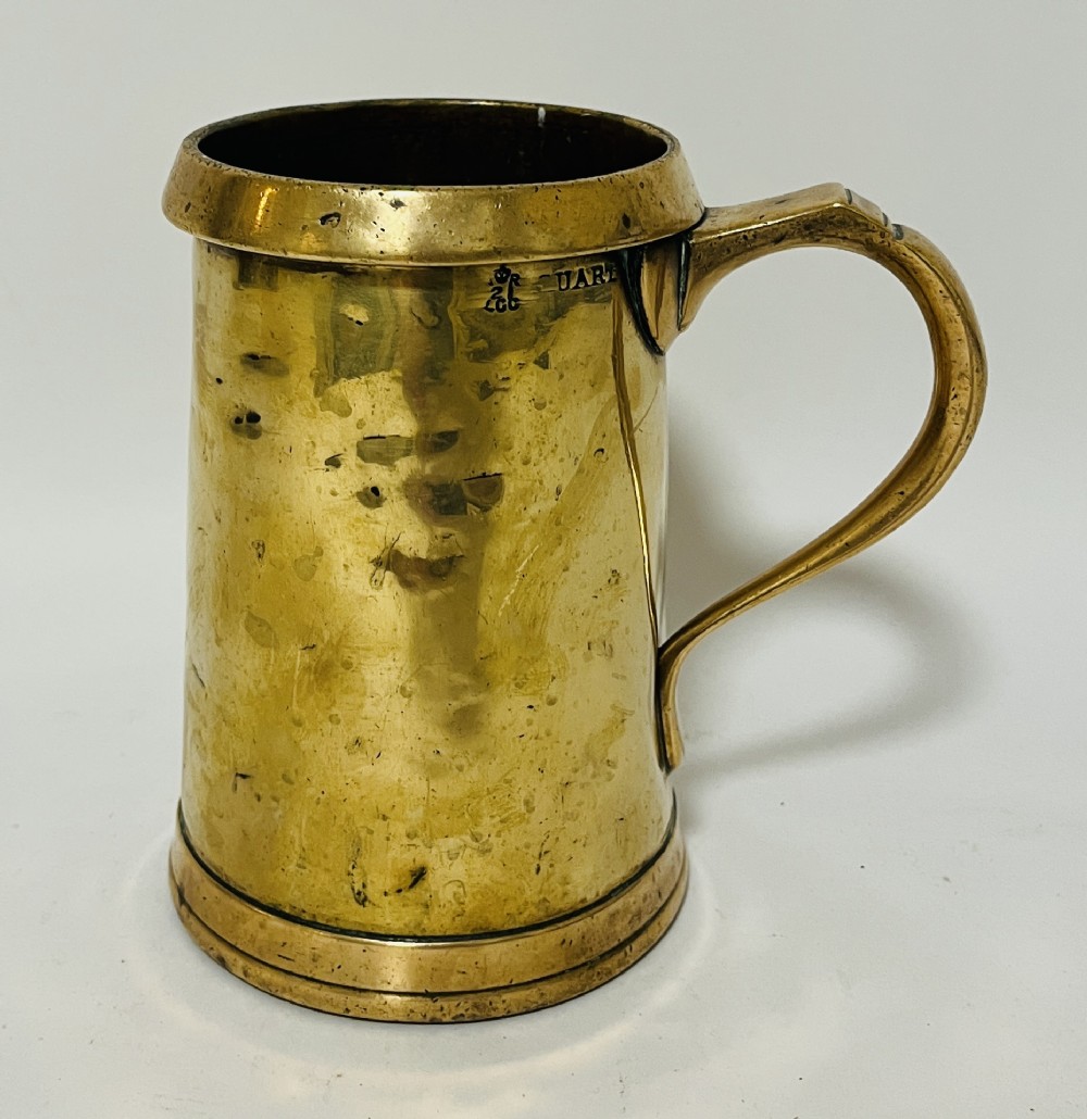 A Victorian brass quart tankard with a curved side handle, stamped verification marks near the rim, and a flared base.