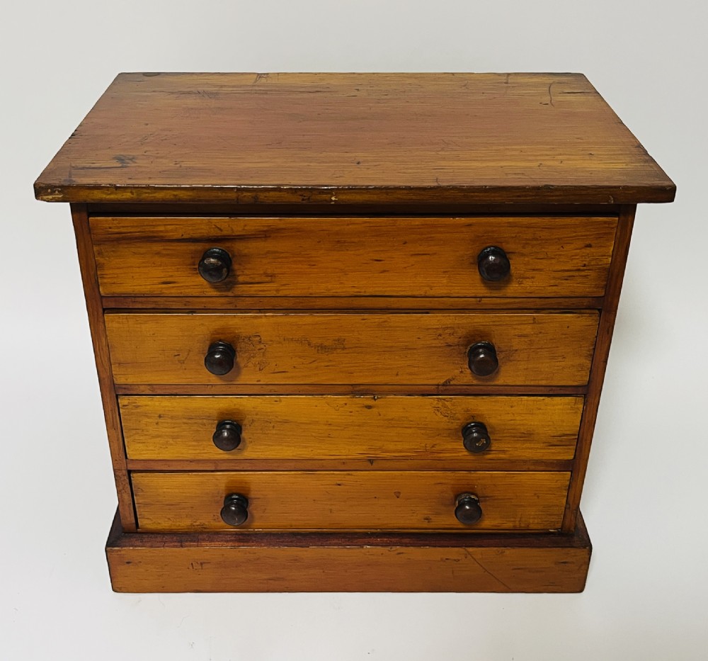 An antique stained pine specimen cabinet featuring four horizontal drawers with turned dark wood knobs and a solid plinth base.
