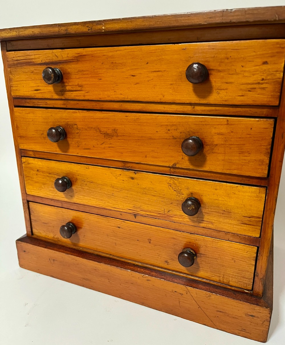 An antique stained pine specimen cabinet featuring four horizontal drawers with turned dark wood knobs and a solid plinth base. View IV