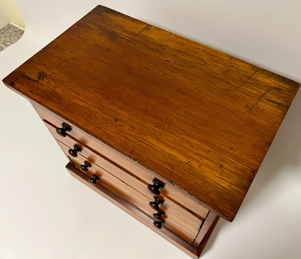 An antique stained pine specimen cabinet featuring four horizontal drawers with turned dark wood knobs and a solid plinth base. View V