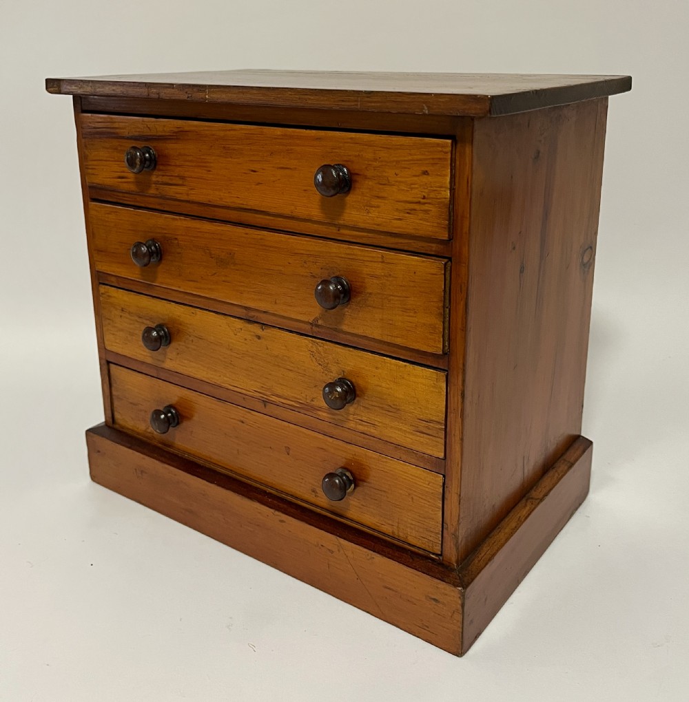 An antique stained pine specimen cabinet featuring four horizontal drawers with turned dark wood knobs and a solid plinth base. View IX