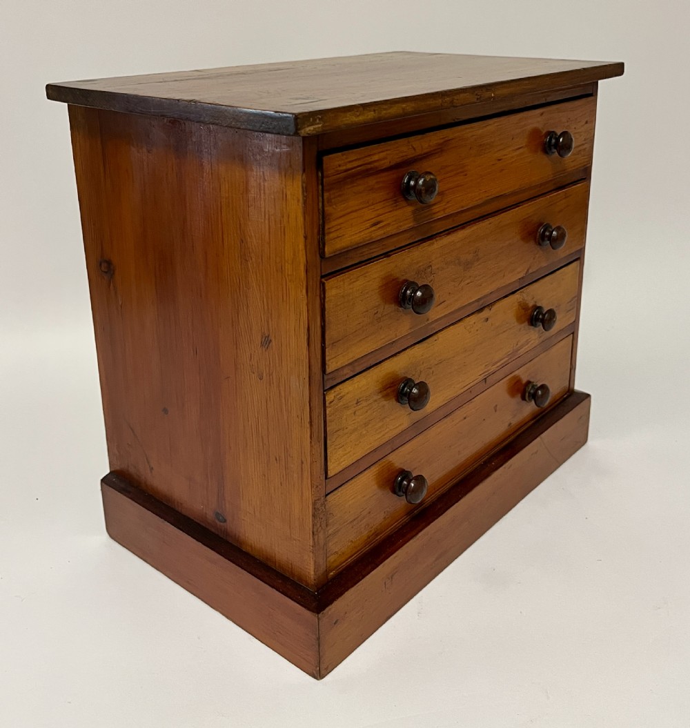 An antique stained pine specimen cabinet featuring four horizontal drawers with turned dark wood knobs and a solid plinth base. View XII