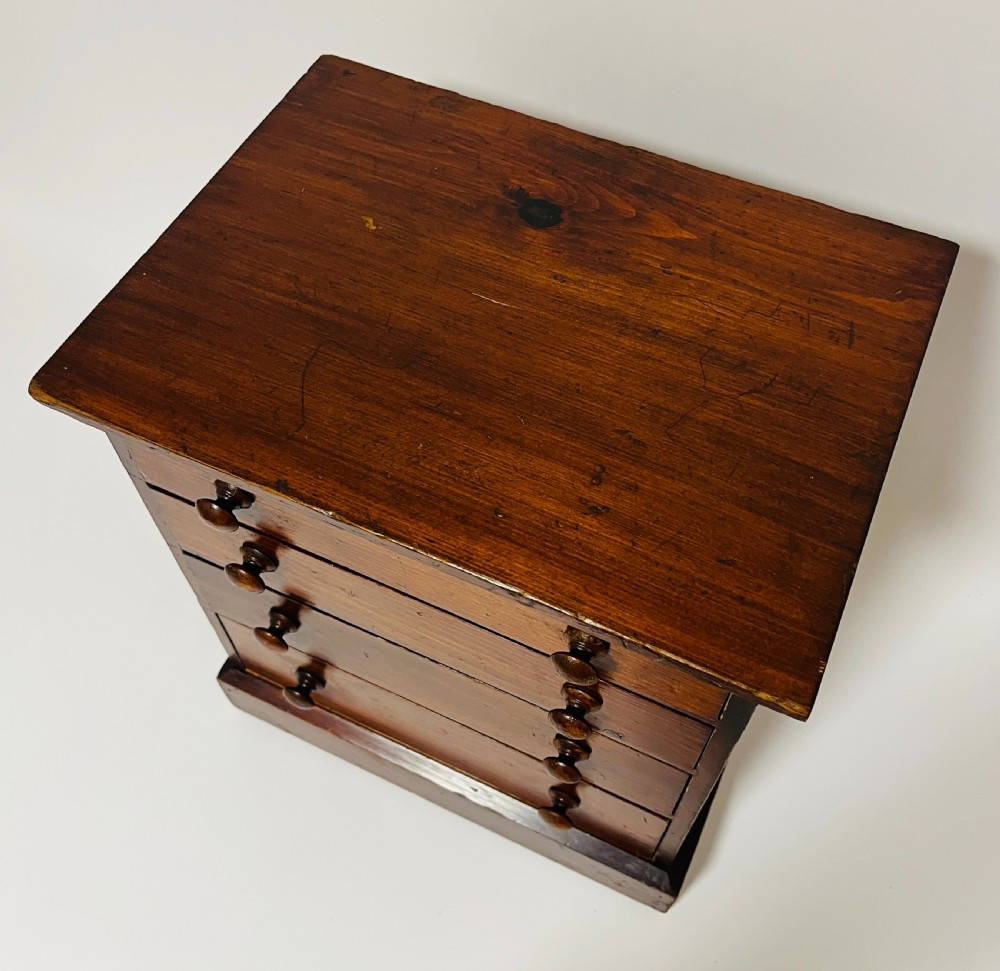 A small antique stained pine tabletop collectors cabinet featuring four drawers with turned wooden knobs on a plinth base. View III