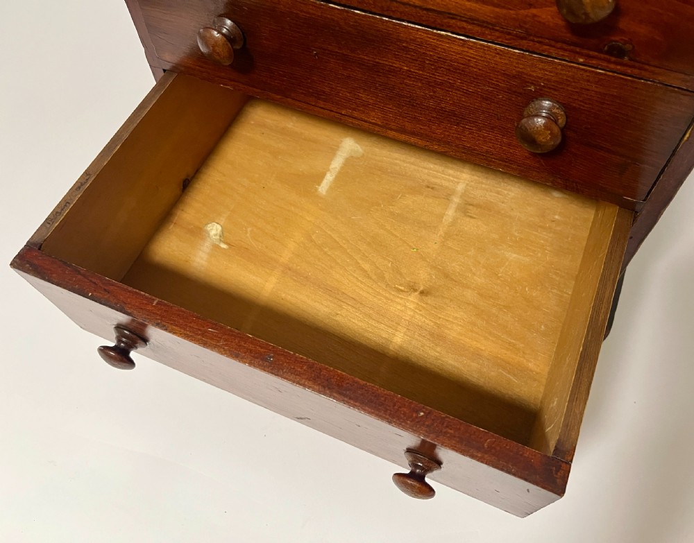 A small antique stained pine tabletop collectors cabinet featuring four drawers with turned wooden knobs on a plinth base. View IV