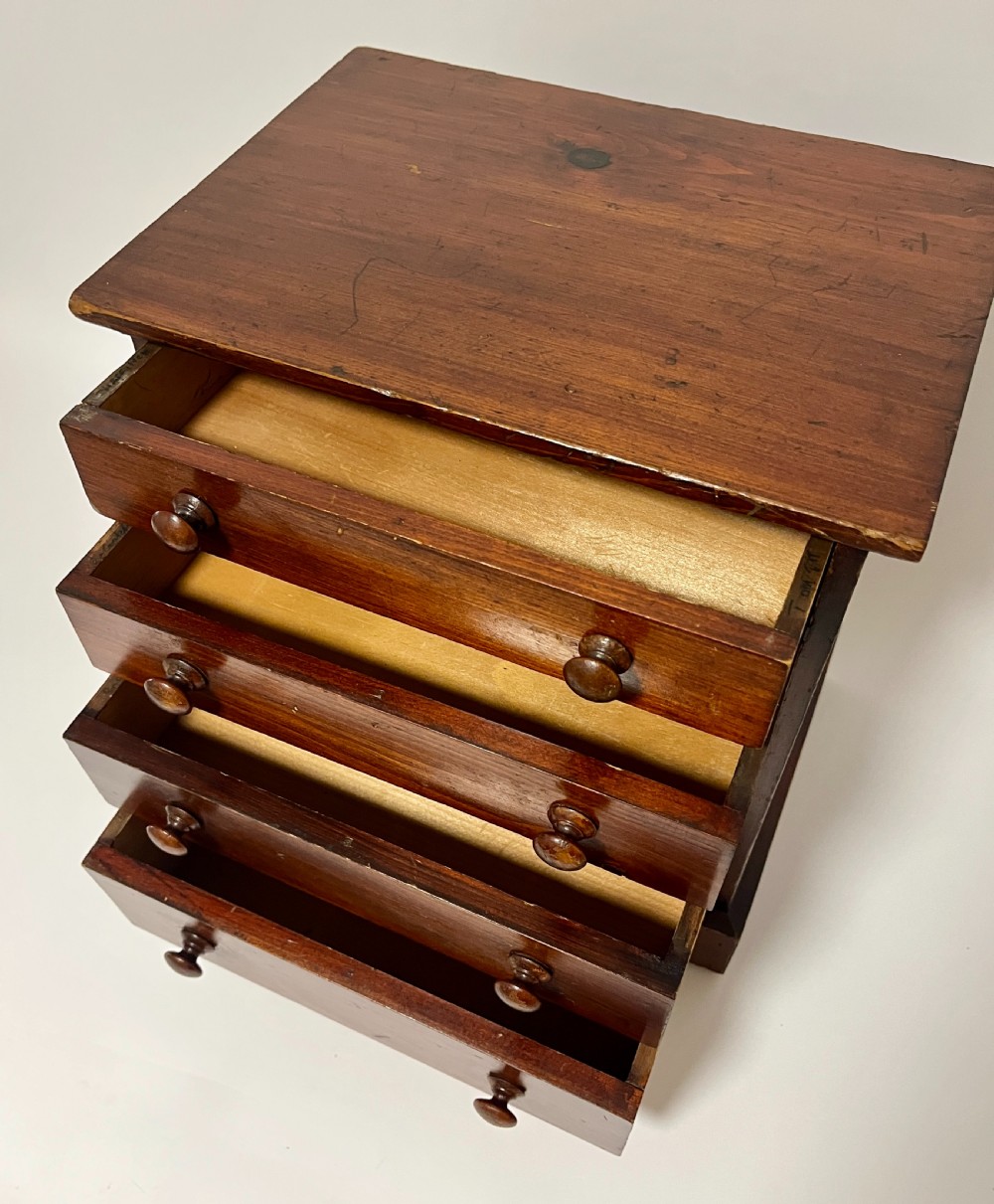A small antique stained pine tabletop collectors cabinet featuring four drawers with turned wooden knobs on a plinth base. View V