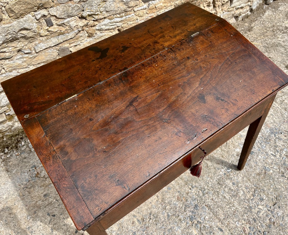 A Georgian solid oak clerks desk featuring a hinged sloped writing top, a key with tassel inserted into the central keyhole, and four square tapered legs. View VIII