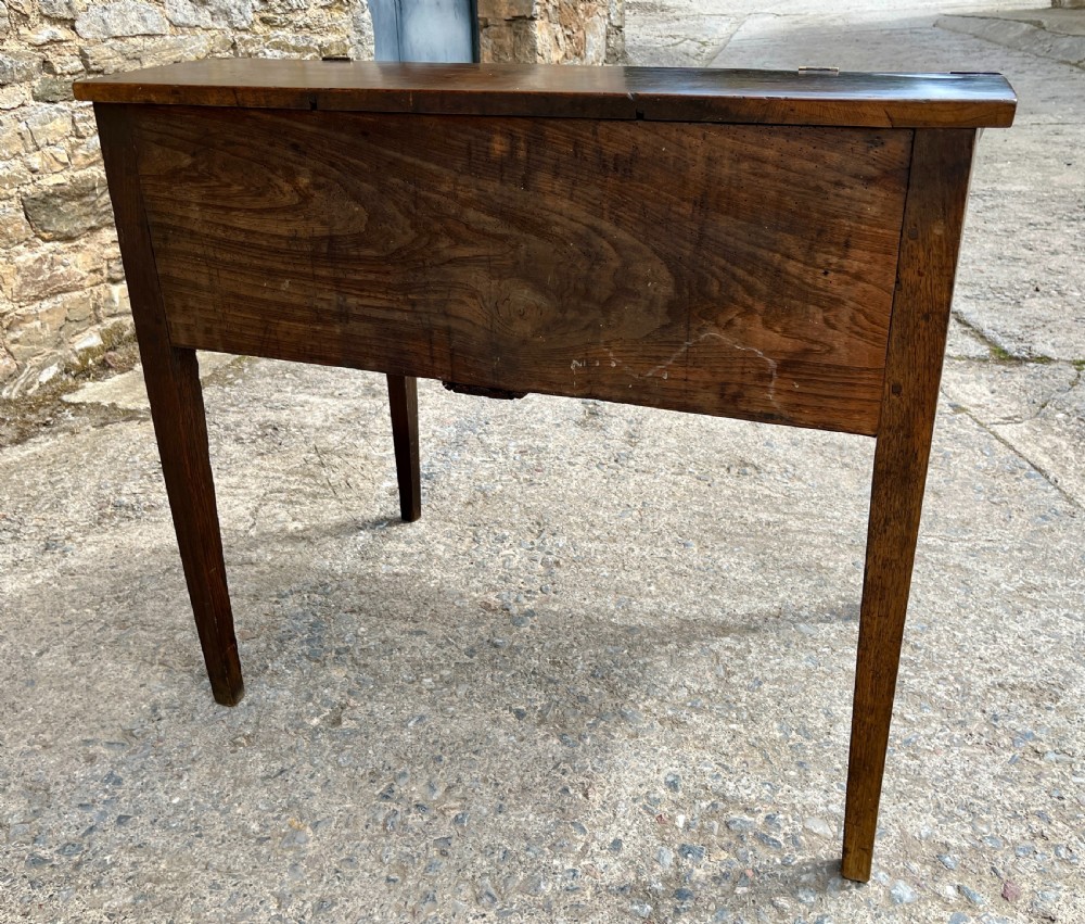 A Georgian solid oak clerks desk featuring a hinged sloped writing top, a key with tassel inserted into the central keyhole, and four square tapered legs. View XIX