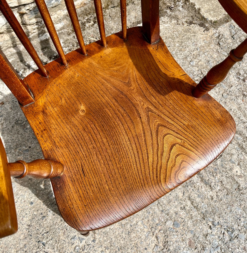 An antique wooden Windsor armchair featuring vertical back spindles, turned legs, curved armrests, and a shaped saddle seat. View II