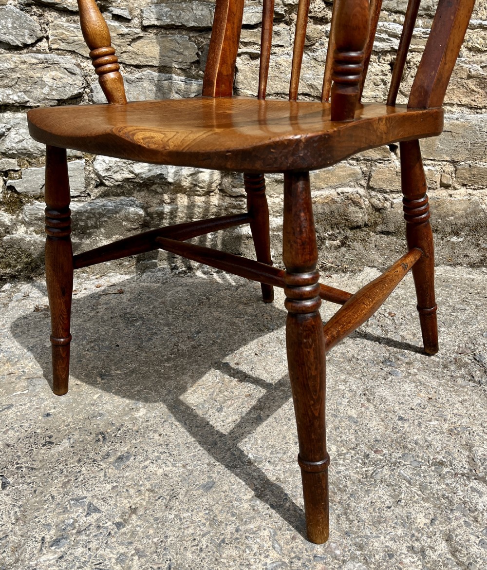 An antique wooden Windsor armchair featuring vertical back spindles, turned legs, curved armrests, and a shaped saddle seat. View IV