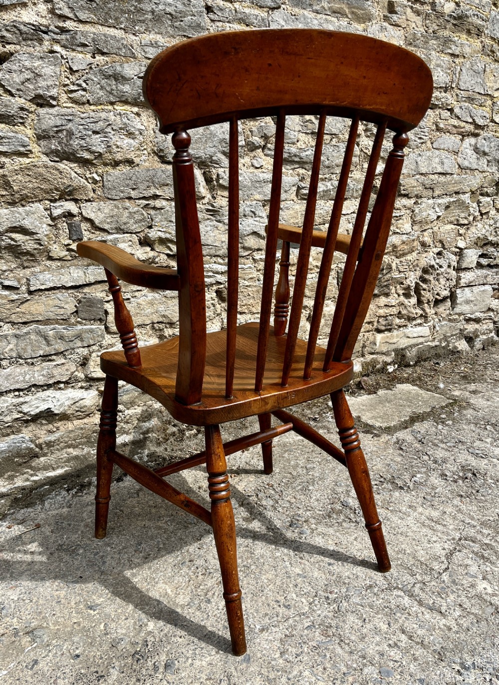 An antique wooden Windsor armchair featuring vertical back spindles, turned legs, curved armrests, and a shaped saddle seat. View VII