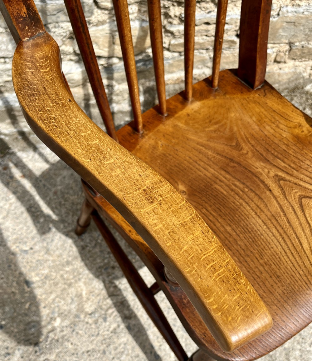 An antique wooden Windsor armchair featuring vertical back spindles, turned legs, curved armrests, and a shaped saddle seat. View X