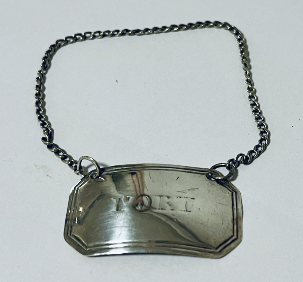 A curved rectangular Georgian silver decanter label engraved with the word PORT, attached to a silver suspension chain.