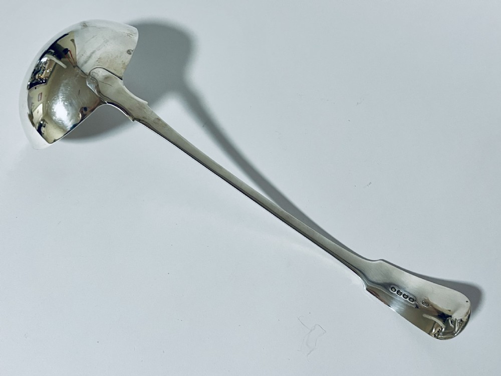 A polished Georgian silver serving ladle featuring a deep circular bowl and a long curved handle resting on a plain light surface. View VIII