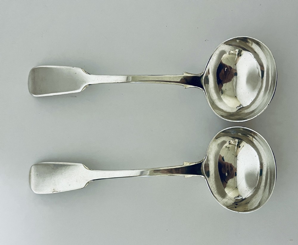 A pair of Georgian sterling silver sauce ladles with fiddle pattern handles and deep circular bowls arranged on a plain surface. View II