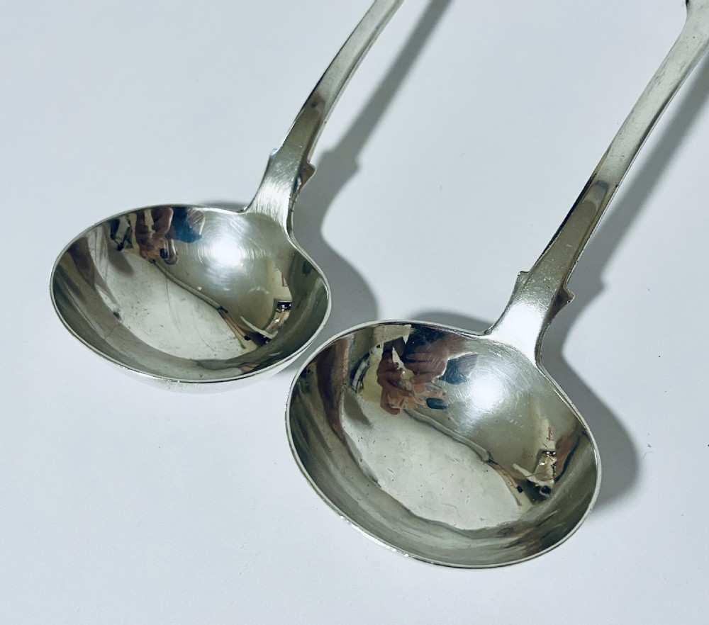 A pair of Georgian sterling silver sauce ladles with fiddle pattern handles and deep circular bowls arranged on a plain surface. View III