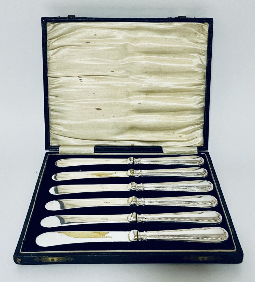 A set of six antique silver-handled butter knives arranged inside a velvet and satin lined presentation case.