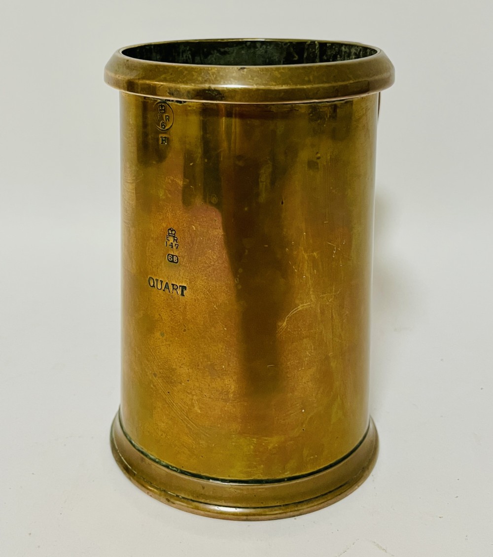 A cylindrical Victorian brass quart measure featuring a rolled rim and official stamped verification marks alongside the word QUART.
