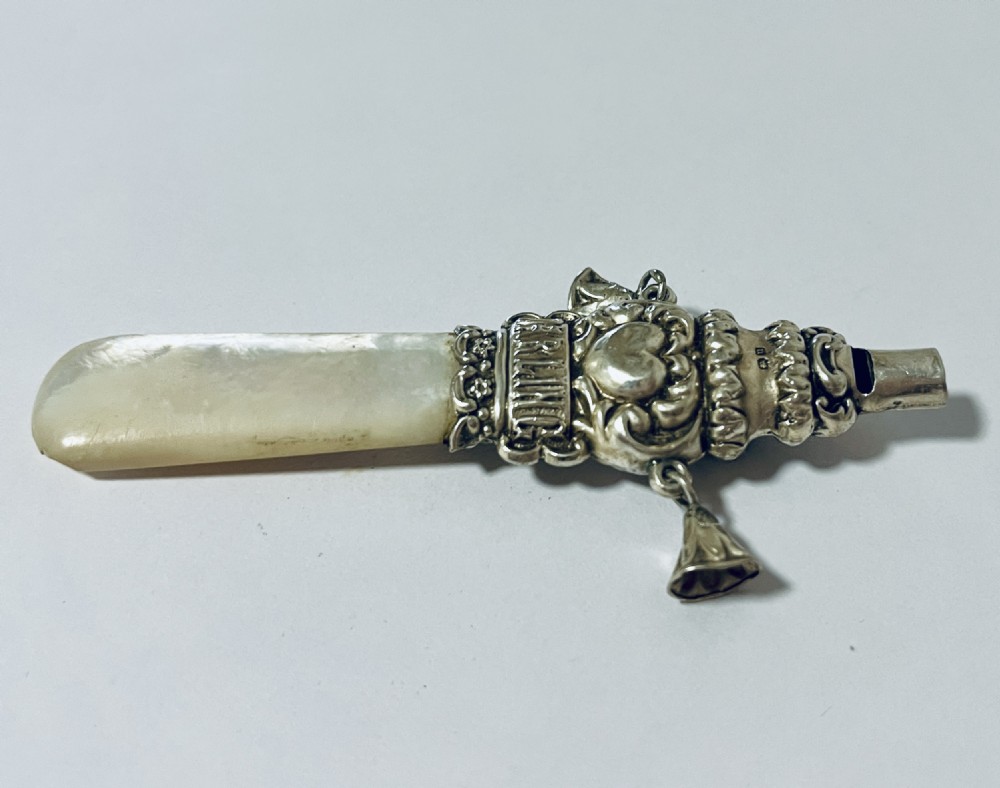 An antique silver baby rattle and teether featuring a flat mother of pearl handle, suspended silver bells, an integrated whistle top, and embossed lettering spelling DARLING. View V