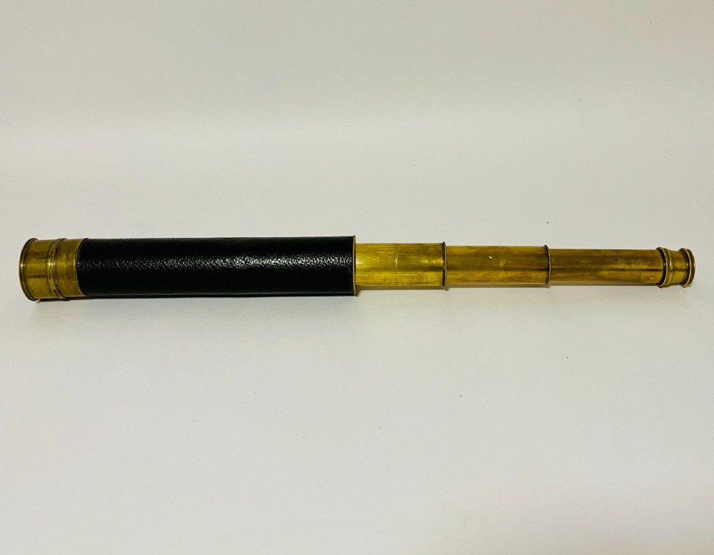 A fully extended three-draw brass telescope featuring a textured black leather sleeve around the main barrel.