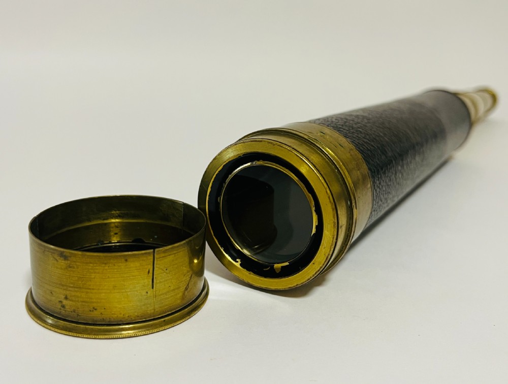 A fully extended three-draw brass telescope featuring a textured black leather sleeve around the main barrel. View V