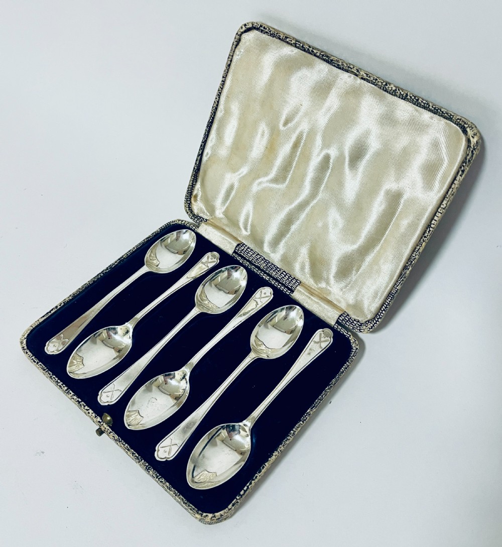 A set of six silver teaspoons with crossed golf club motifs on the handles, arranged inside an open satin and velvet lined presentation case.