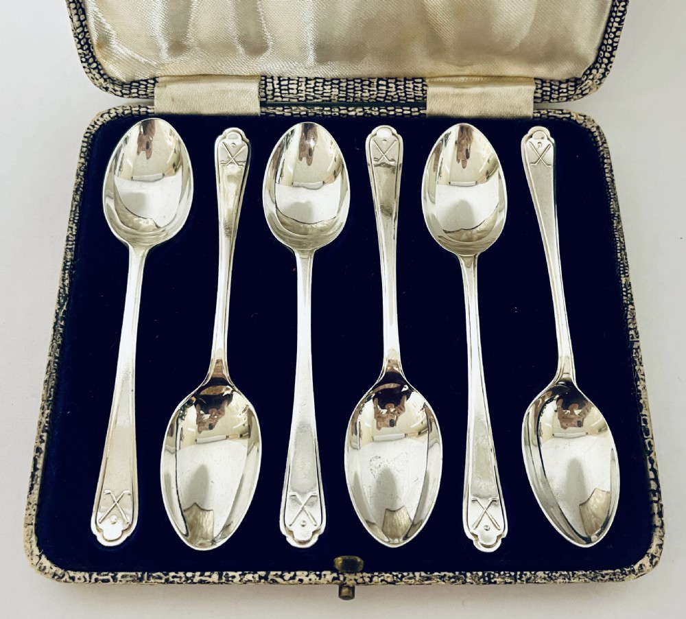 A set of six silver teaspoons with crossed golf club motifs on the handles, arranged inside an open satin and velvet lined presentation case. View II
