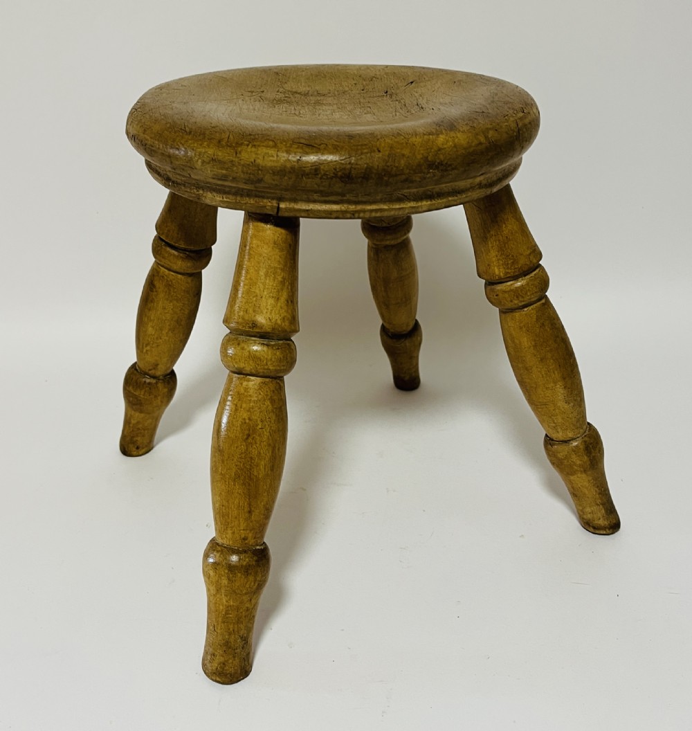 A small antique wooden hearth stool featuring a circular dished seat supported by four splayed turned legs.